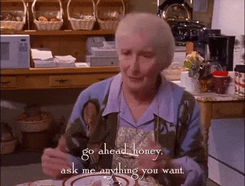 Older woman sitting at a kitchen table saying "Go ahead, honey, ask me anything you want."